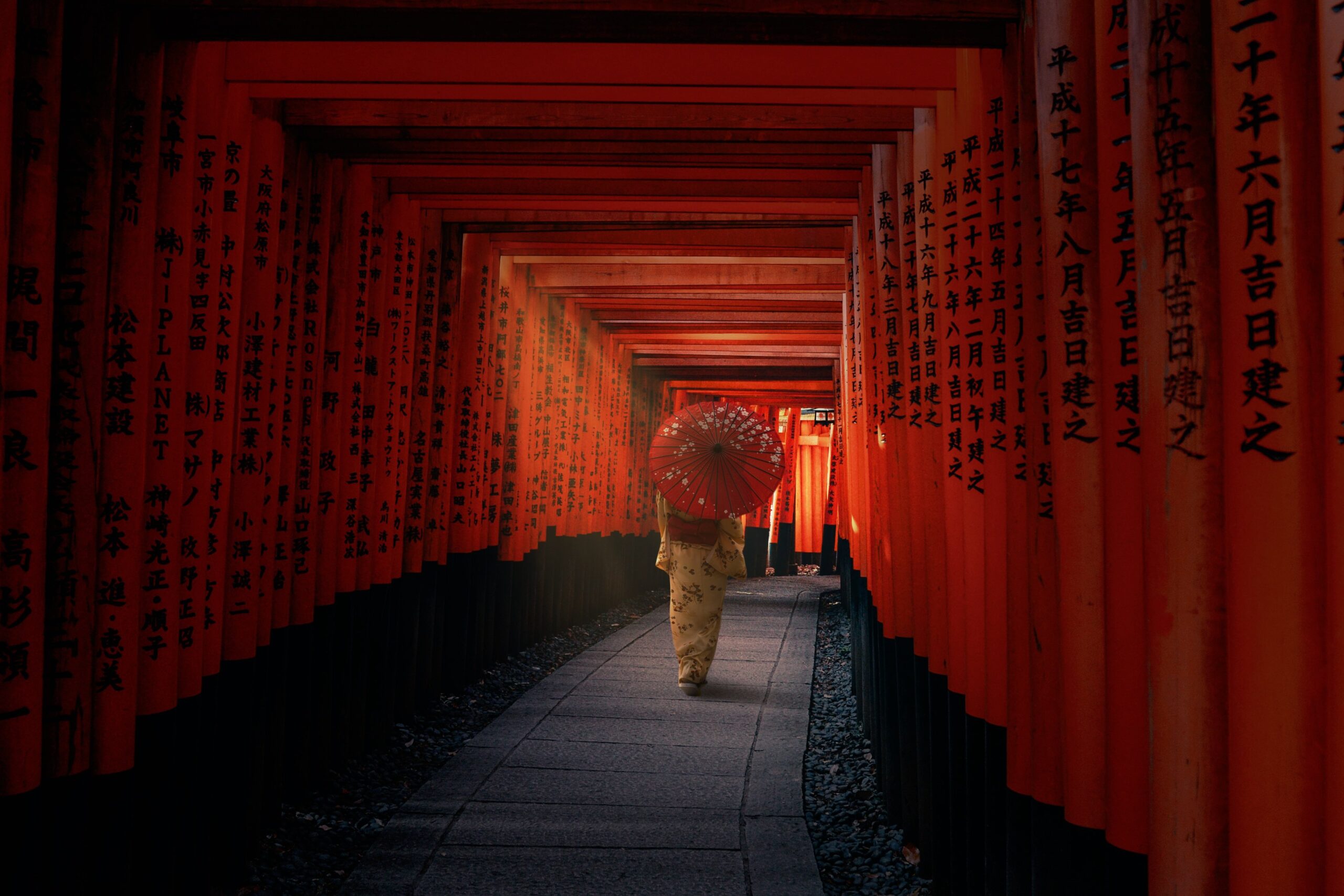 Person carrying a traditional umbrella beneath the red torii gates at Fushimi Inari shrine in Kyoto