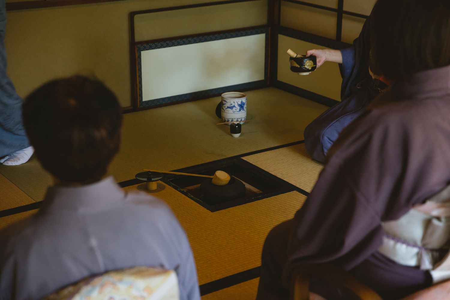 Guests in kimono seated around a sunken hearth during a Japanese tea gathering in Kyoto