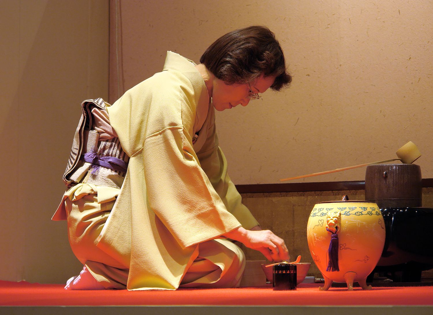 Tea practitioner in a pale yellow kimono preparing utensils for a Japanese tea ceremony